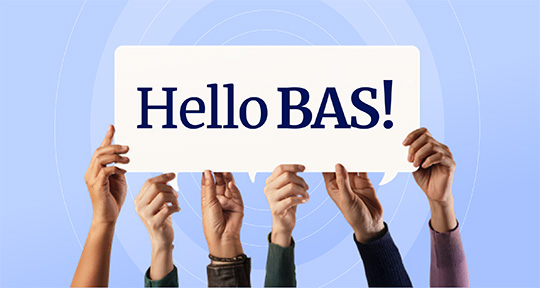 A man sitting behind a laptop with the text 'Hello Bas' on the screen.