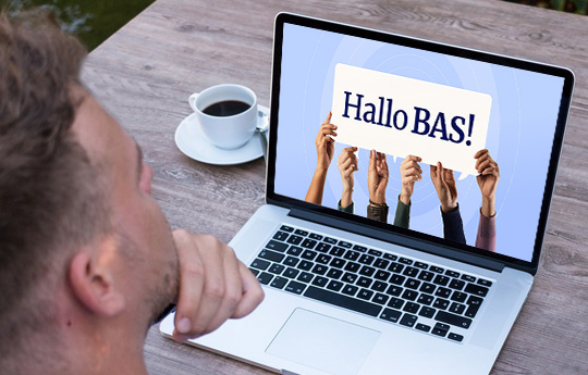 Een man achter een laptop met op het scherm de tekst 'Hallo Bas'