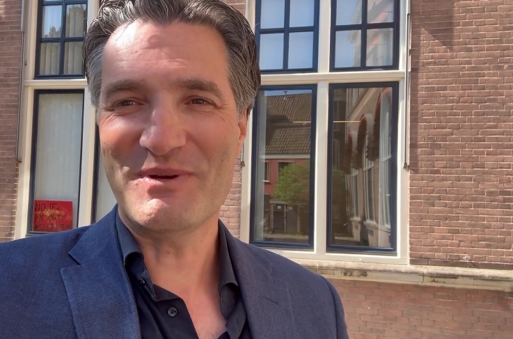 A man looks into the camera. In the background, the windows of a historic building.